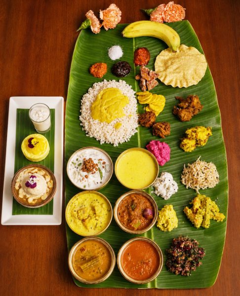 Banana leaf thali with rice and a variety of curries, chutneys, sweets, papad, and a banana on top right.